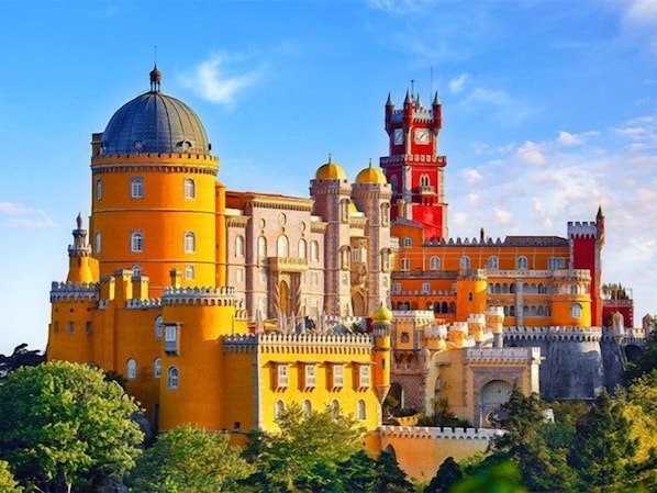 Un edificio grande e histórico con múltiples torres y cúpulas, rodeado de abundante vegetación.