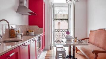 Una cocina moderna con una pared de acento roja, un área de comedor con una mesa blanca y un sofá rosa, y una vista a través de una puerta abierta.