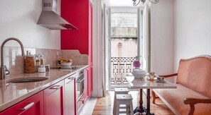 Una cocina moderna con una pared de acento roja, un área de comedor con una mesa blanca y un sofá rosa, y una vista a través de una puerta abierta.