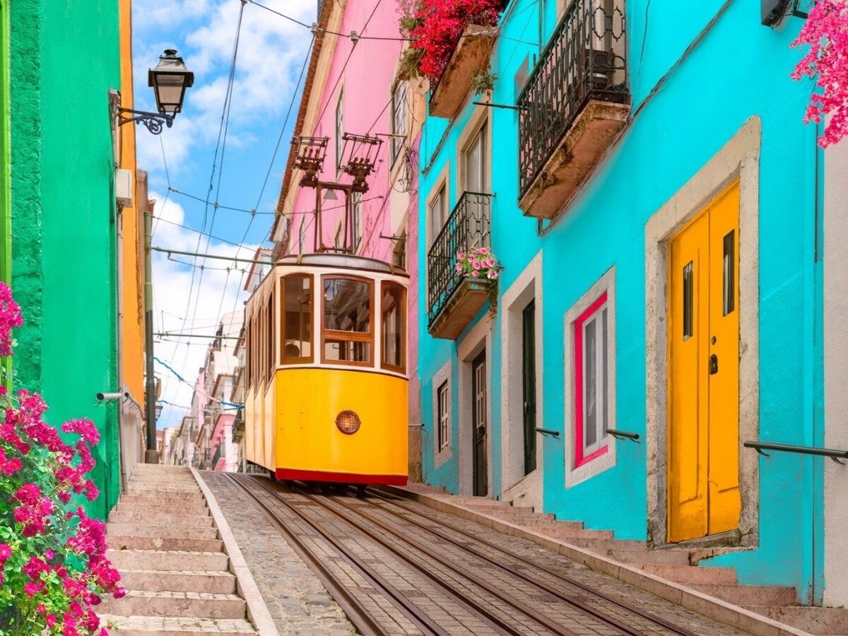 A yellow tram on a narrow street flanked by colorful buildings with balconies and flower boxes.