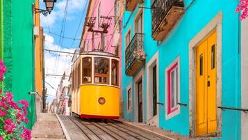 A yellow tram on a narrow street flanked by colorful buildings with balconies and flower boxes.