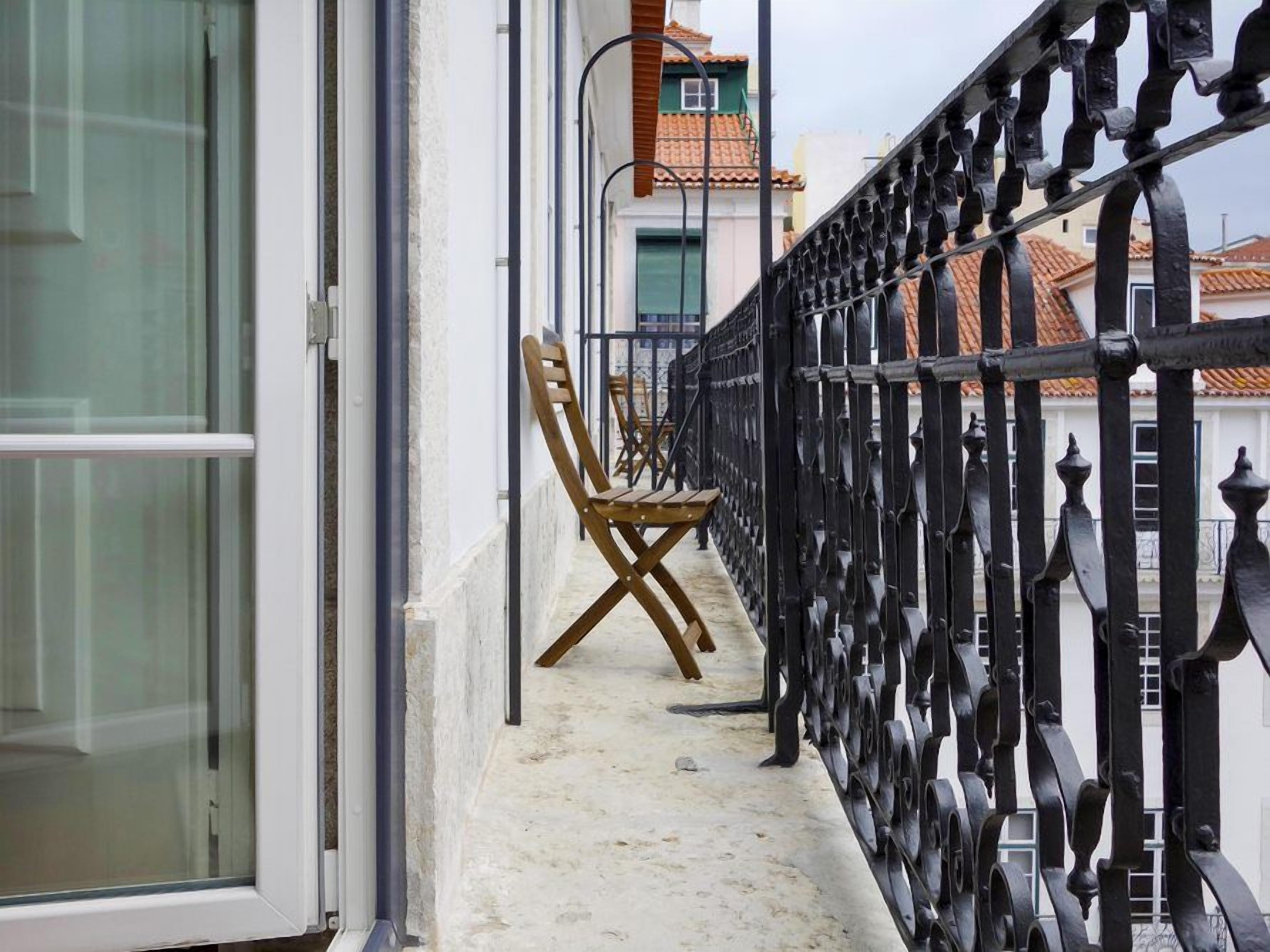 A balcony with a metal railing, a wooden chair, and a window.