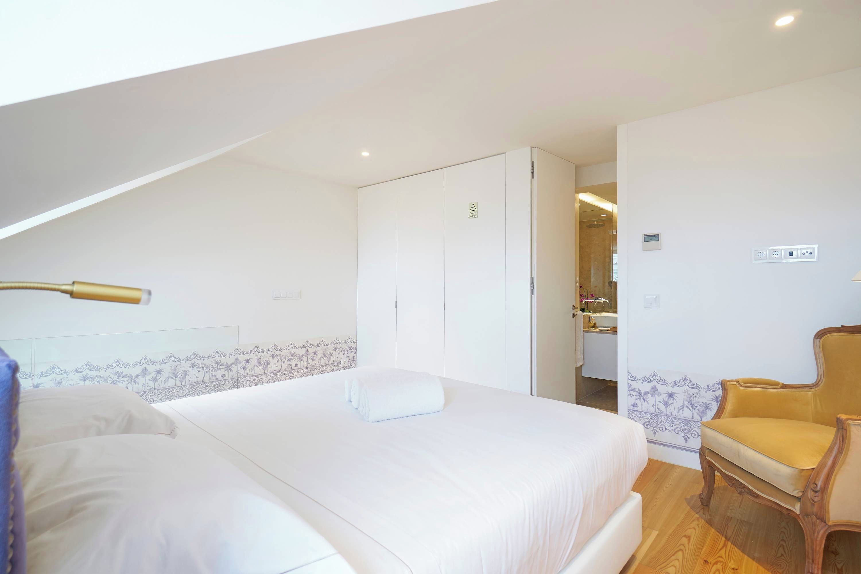 Ein Schlafzimmer mit einem Bett, einem Sessel und einem durch eine offene Tür einsehbaren Badezimmer.