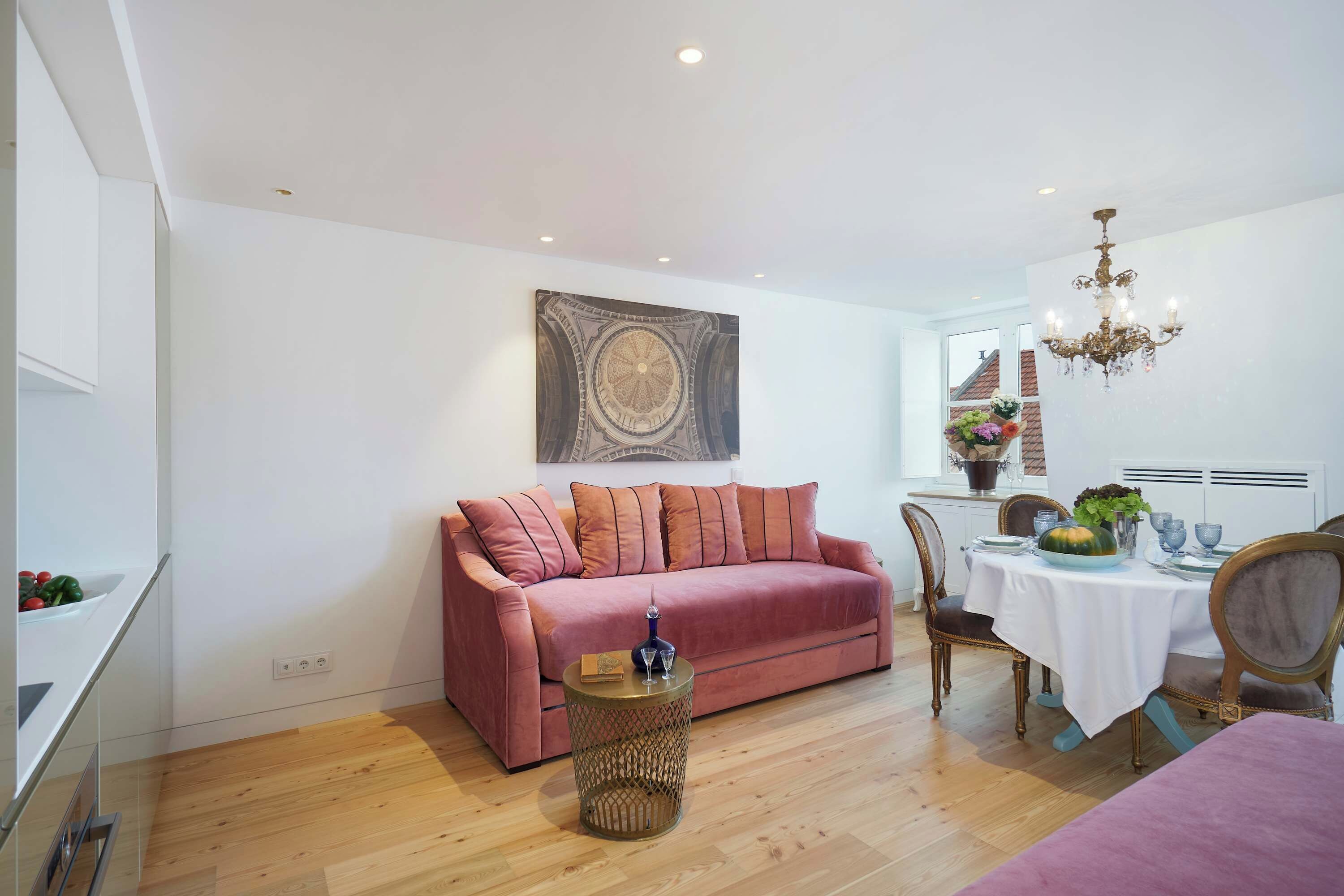 Ein modernes Wohnzimmer mit einem rosa Sofa, einem Esstisch für vier Personen und einer Kristallleuchtre.