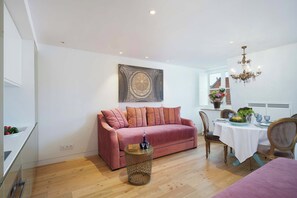 Ein modernes Wohnzimmer mit einem rosa Sofa, einem Esstisch für vier Personen und einer Kristallleuchtre.