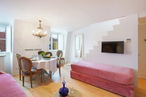 Ein modernes Wohnzimmer mit Essbereich, einem pinken Sofa, einer Kristallleuchter und einem Wand-Fernseher.