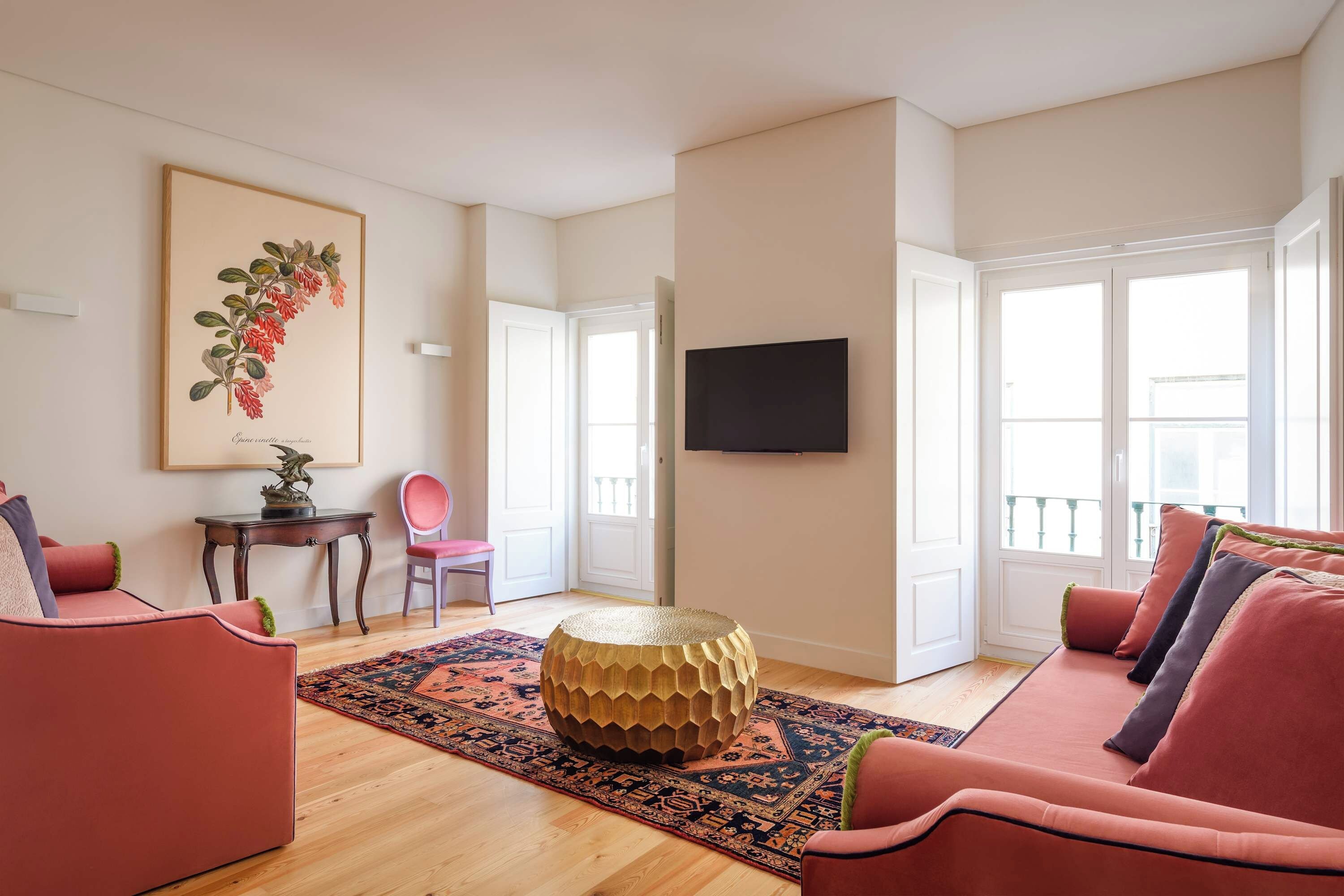 Una sala de estar moderna con una mesa de centro de madera, un sofá rojo, una alfombra estampada y un cuadro en la pared.