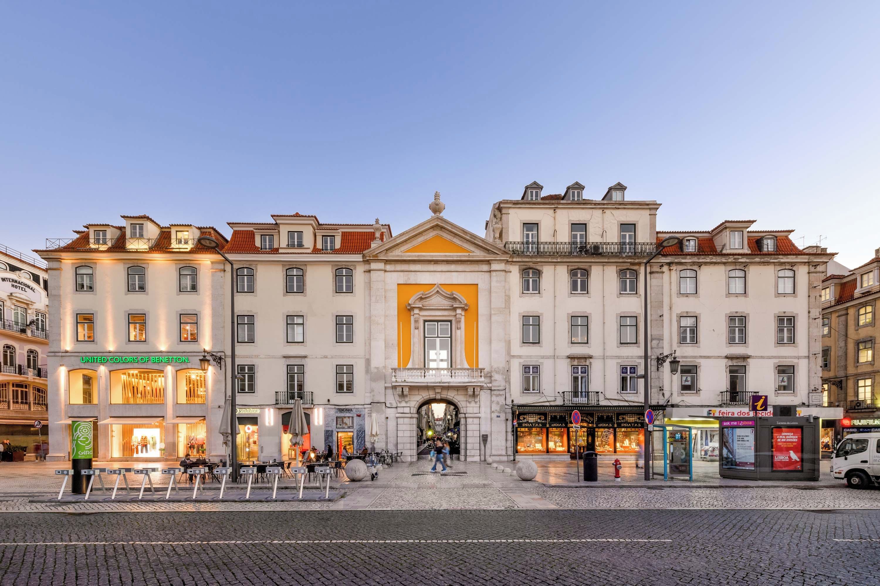 Um edifício histórico com entrada central, vários andares e uma série de lojas no andar térreo.