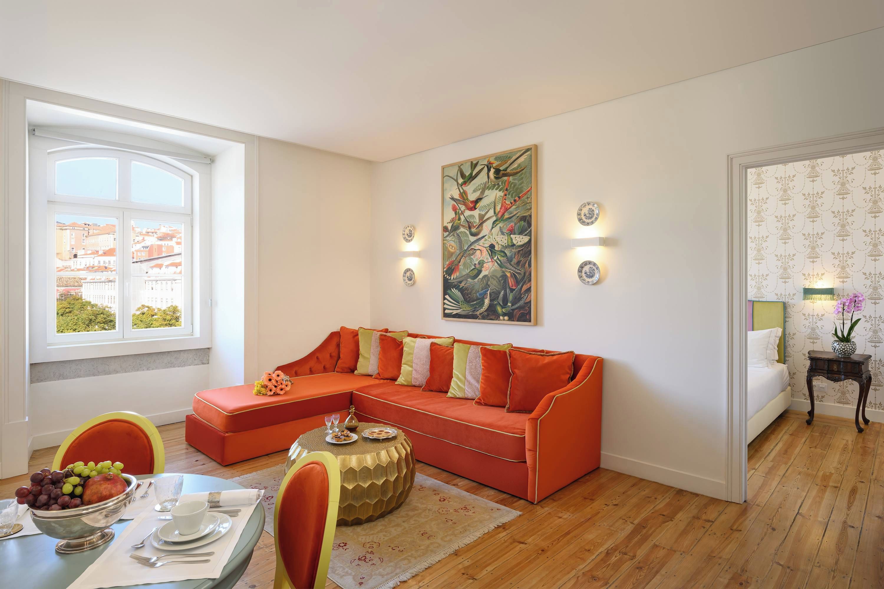 Una sala moderna con un sofá modular, una zona de comedor con una mesa dispuesta para dos personas, y un ventanal con vistas a edificios.