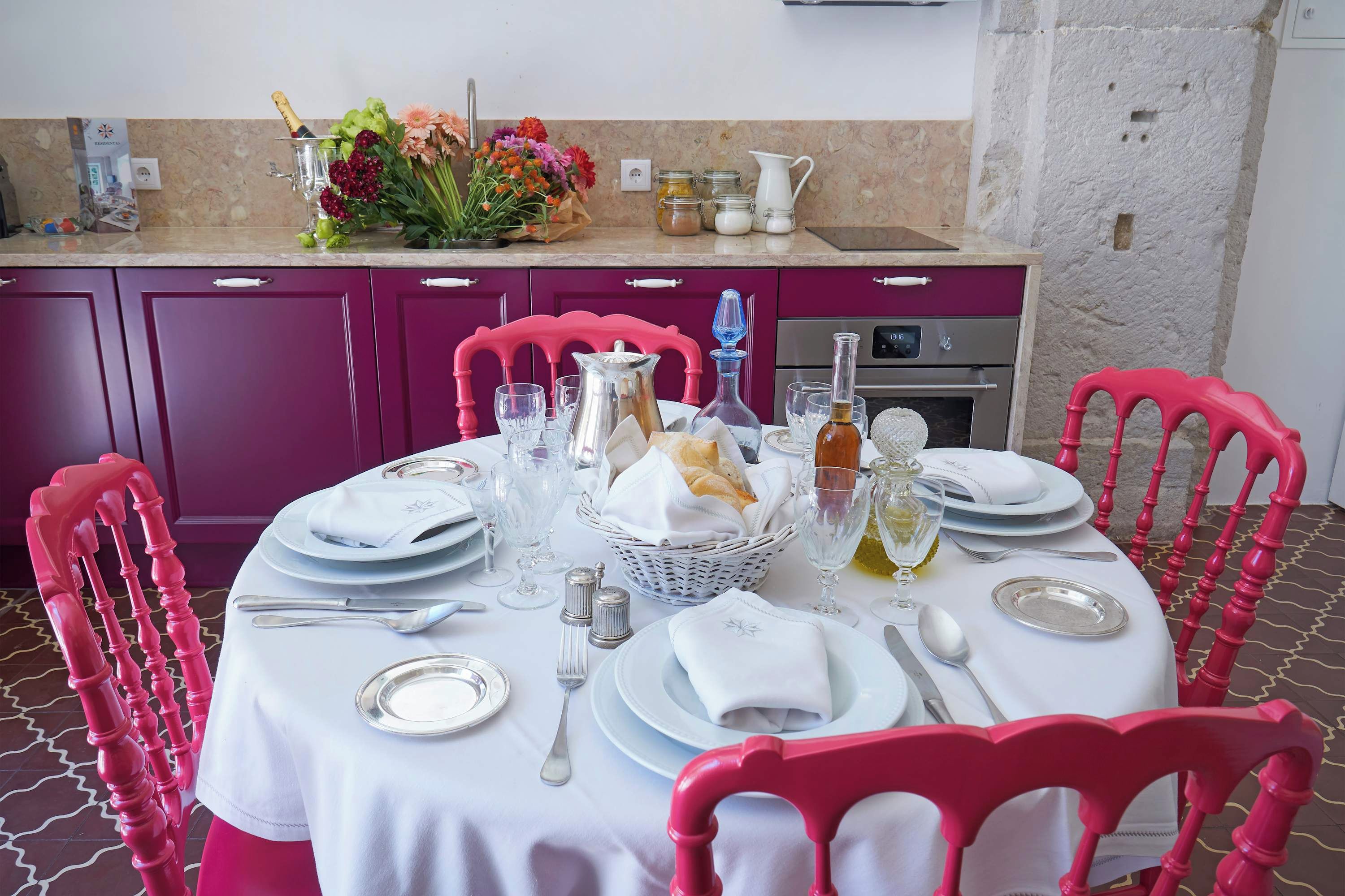 A dining table set with plates, glasses, and cutlery, surrounded by pink chairs.