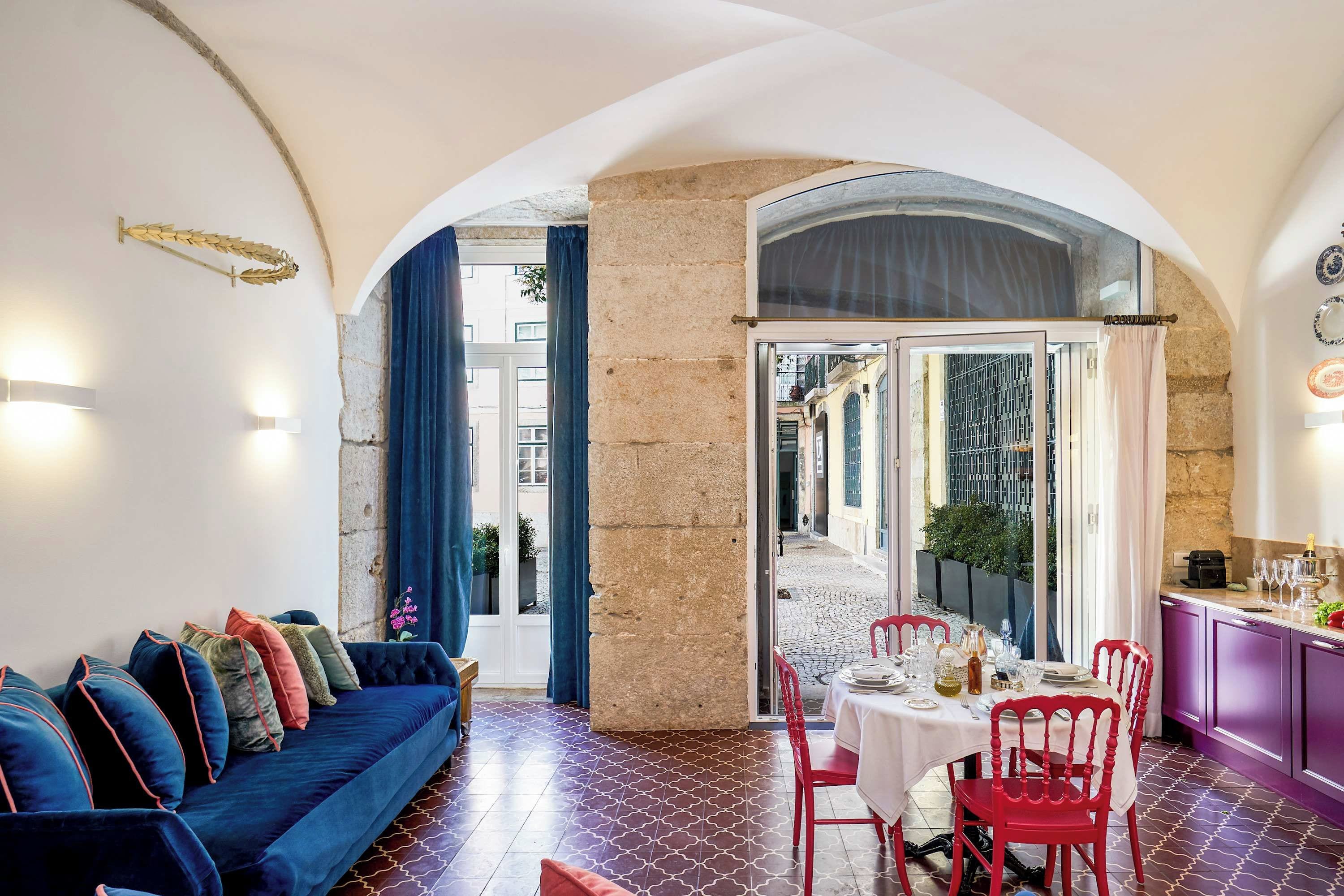A dining area with a table set for two, a blue sofa with cushions, and a stone wall.
