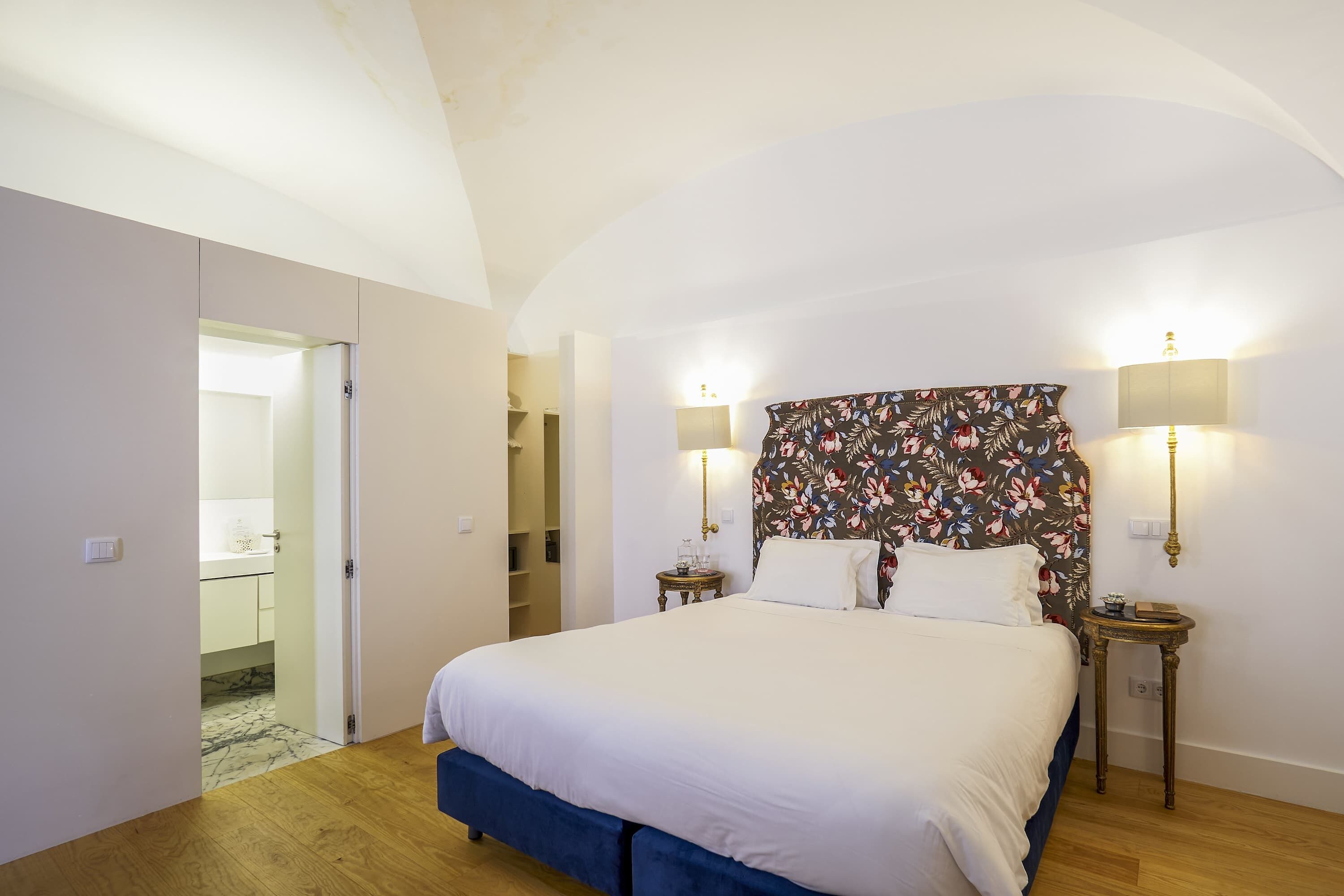 A bedroom with a large bed, two bedside lamps, a floral headboard, and a wardrobe.