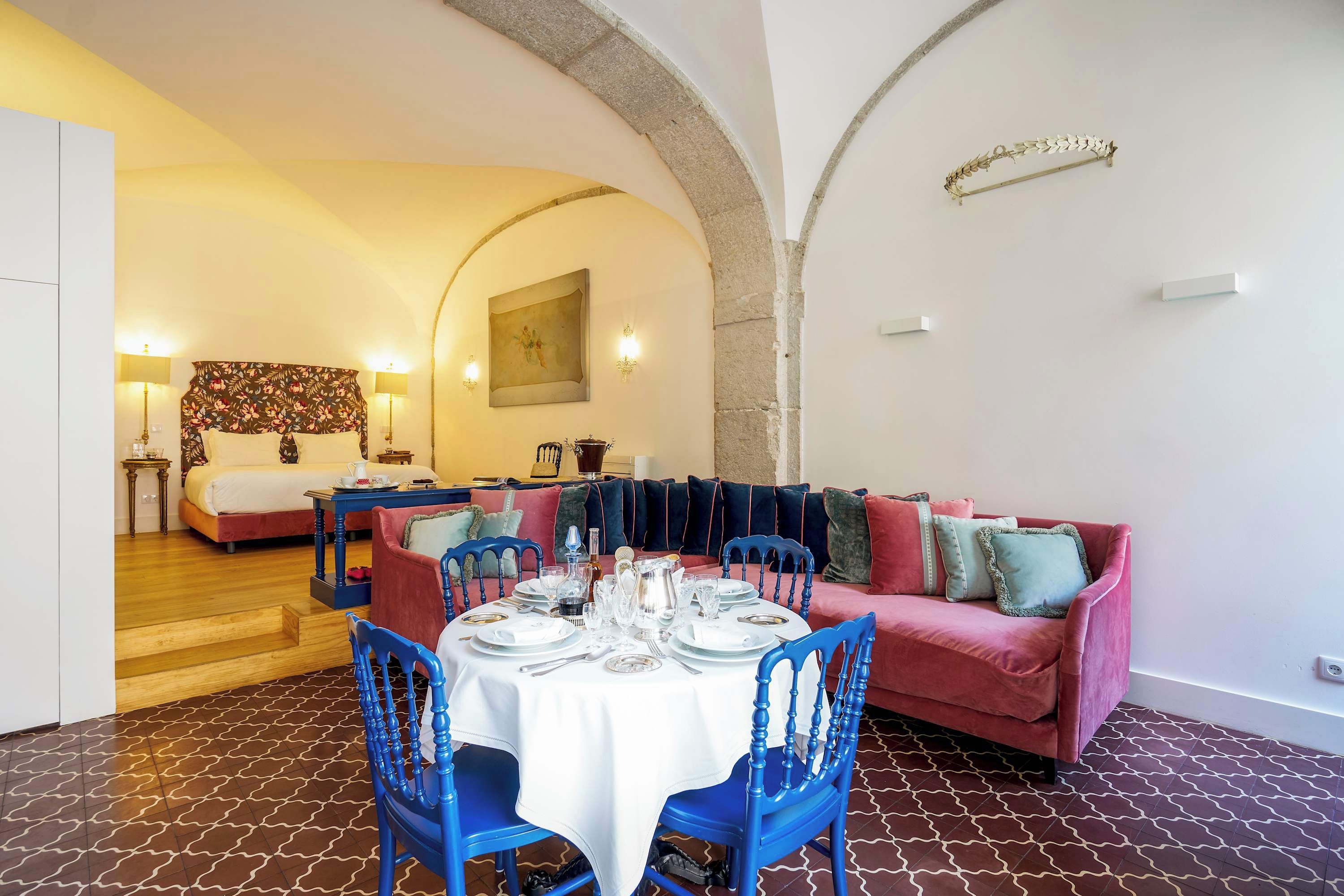 A dining area with a round table set for four, blue chairs, and a red sofa with cushions.