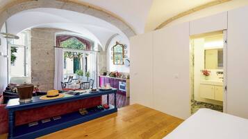 Una habitación con piso de madera, una mesa de comedor con sillas, una zona de cocina con armarios morados y un baño con lavamanos amarillo.
