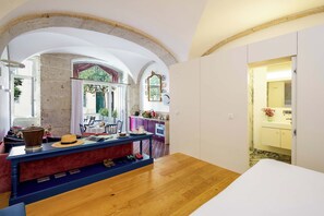 Una habitación con piso de madera, una mesa de comedor con sillas, una zona de cocina con armarios morados y un baño con lavamanos amarillo.