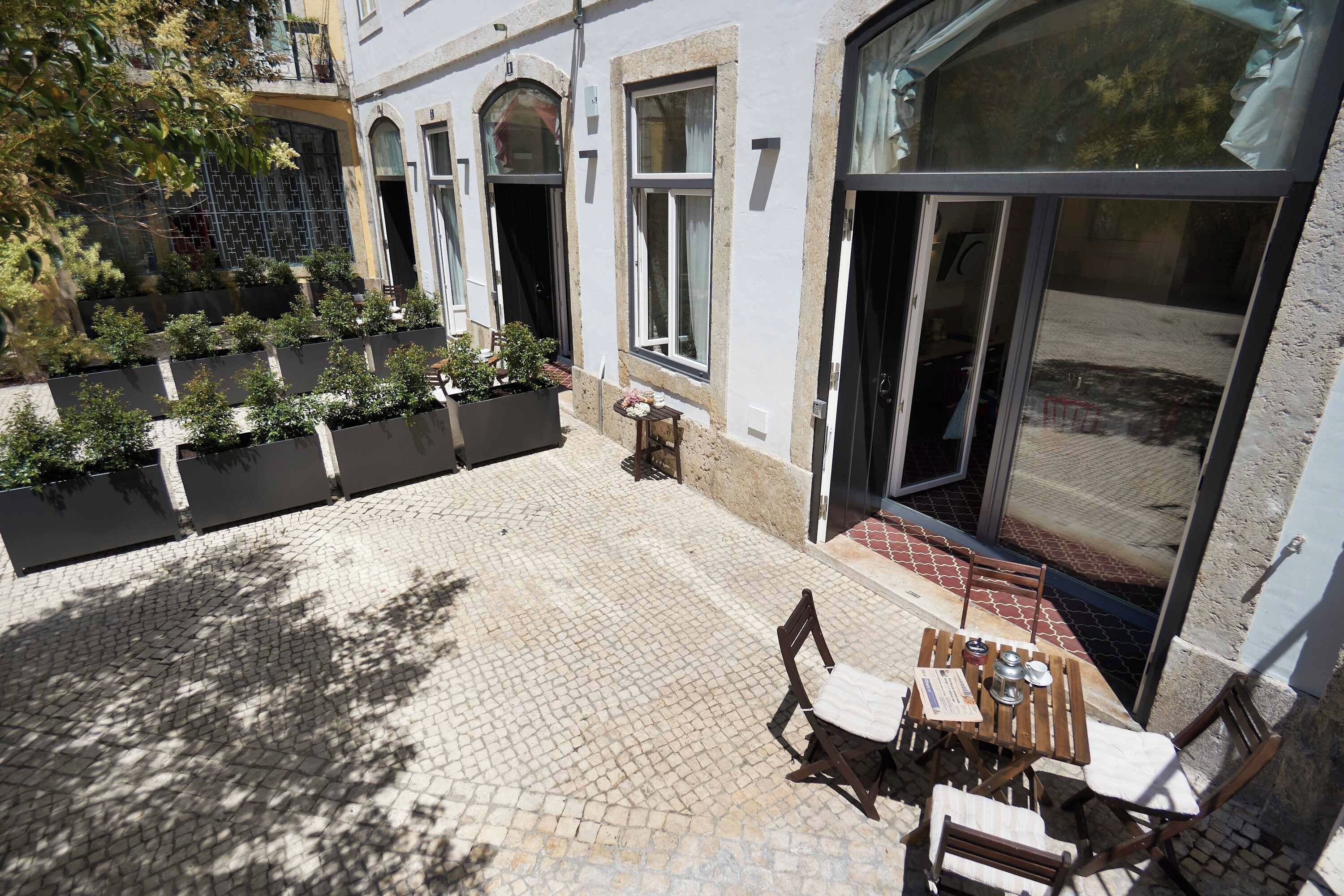 Un patio con suelo empedrado, mobiliario exterior y un gran ventanal corredera.