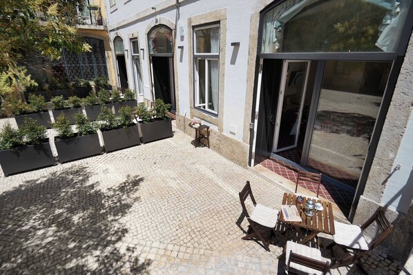 Un patio con suelo empedrado, mobiliario exterior y un gran ventanal corredera.