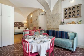 Un comedor con una mesa redonda dispuesta para cuatro, un sofá color turquesa y una cocina al fondo.