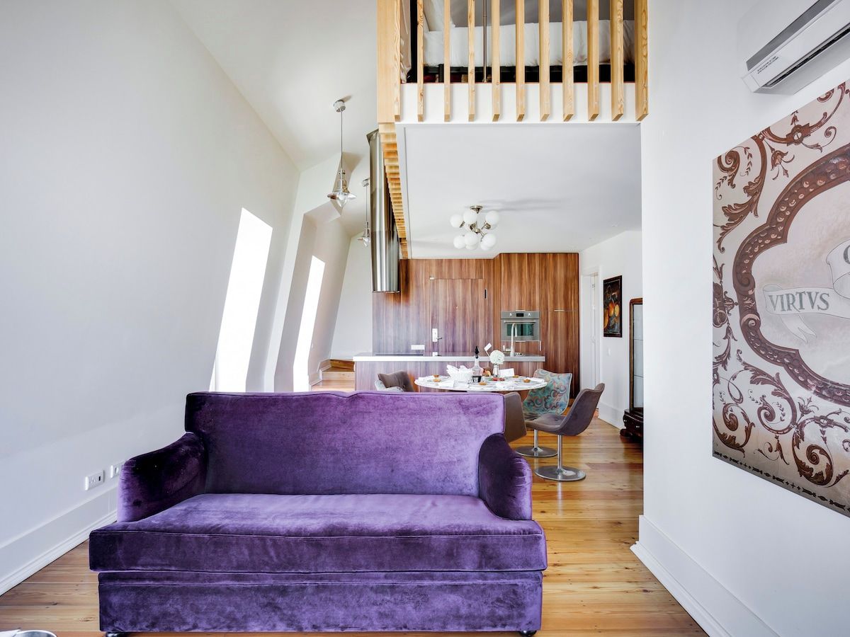Ein modernes Wohnzimmer mit einem violetten Sofa, einem Essbereich mit einem runden Tisch und einer Küche im Hintergrund.