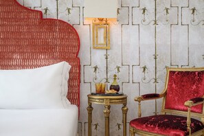 A room with a white upholstered headboard, a red accent wall, a gold-framed side table with a vase and candle, and a red velvet chair. - Rossio View One-Bedroom Apartment in Lisbon (Lisbon)