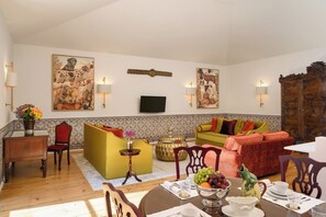 A living room with a sofa set, a dining table with a fruit bowl, and a television mounted on the wall. - Rossio View One-Bedroom Apartment in Lisbon (Lisbon)