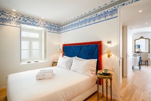 Habitación de hotel con una cama grande, una ventana con persianas, una mesita de noche con lámpara y un espejo en la pared.
