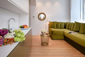 Un espacio de estar moderno con zona de cocina, un sofá verde y una pequeña mesita con objetos decorativos.