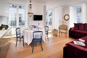 Un comedor con una mesa dispuesta para dos personas, dos sillas, una araña y un televisor montado en la pared.