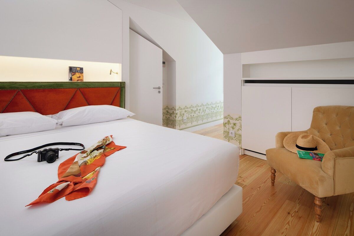 Quarto de hotel com cama, cadeira, câmera e chapéu.