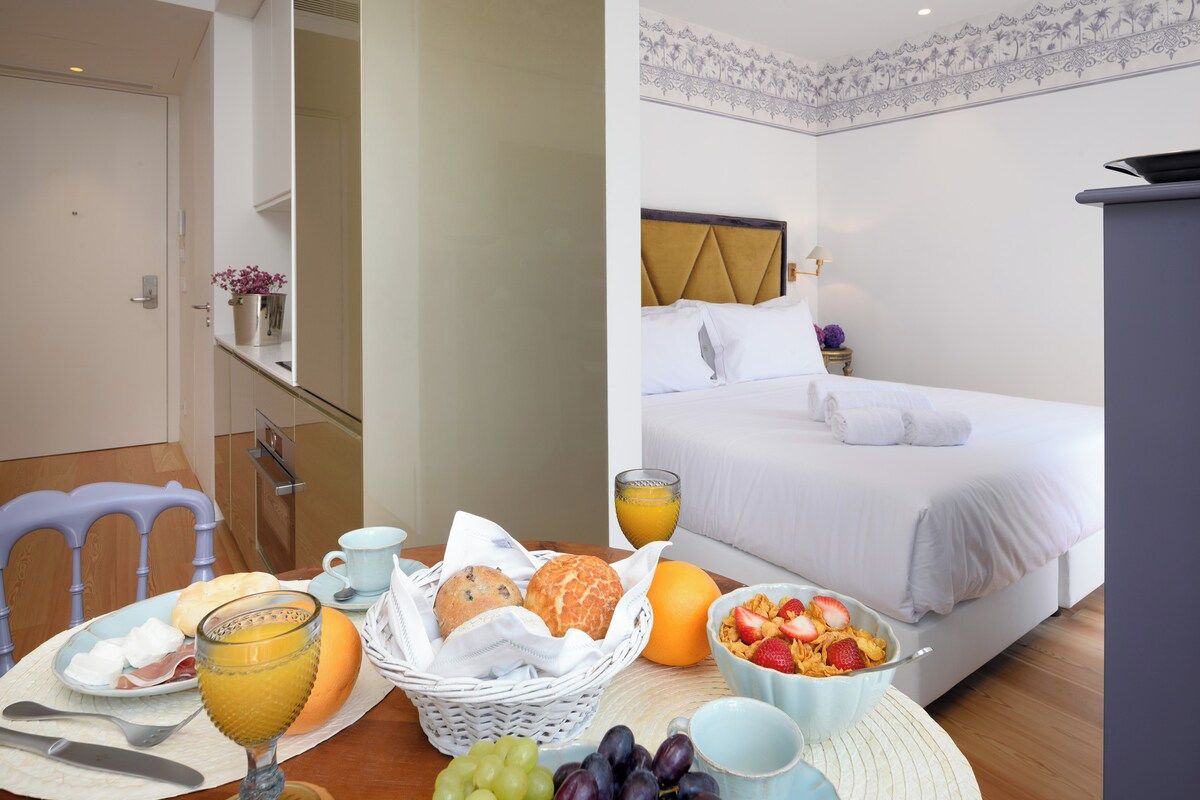 Ein Hotelzimmer mit Bett, Frühstückstisch mit Früchten und Gebäck sowie einem im Hintergrund sichtbaren Badezimmer.