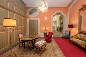 A room with a round table, red armchairs, a sofa, and a chandelier. - Presidential Suite with Rossio Square Views (Lisbon)