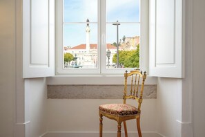 A room with a white wall, a window with a view of a cityscape, and a wooden chair with a patterned cushion. - Presidential Suite with Rossio Square Views (Lisbon)