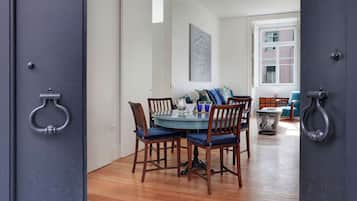 A dining area with a round table and chairs, a window with a view of buildings, and a door with a metal handle.