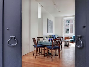 A dining area with a round table and chairs, a window with a view of buildings, and a door with a metal handle. - Historic Lisbon Apartment Near Chiado (Lisbon)