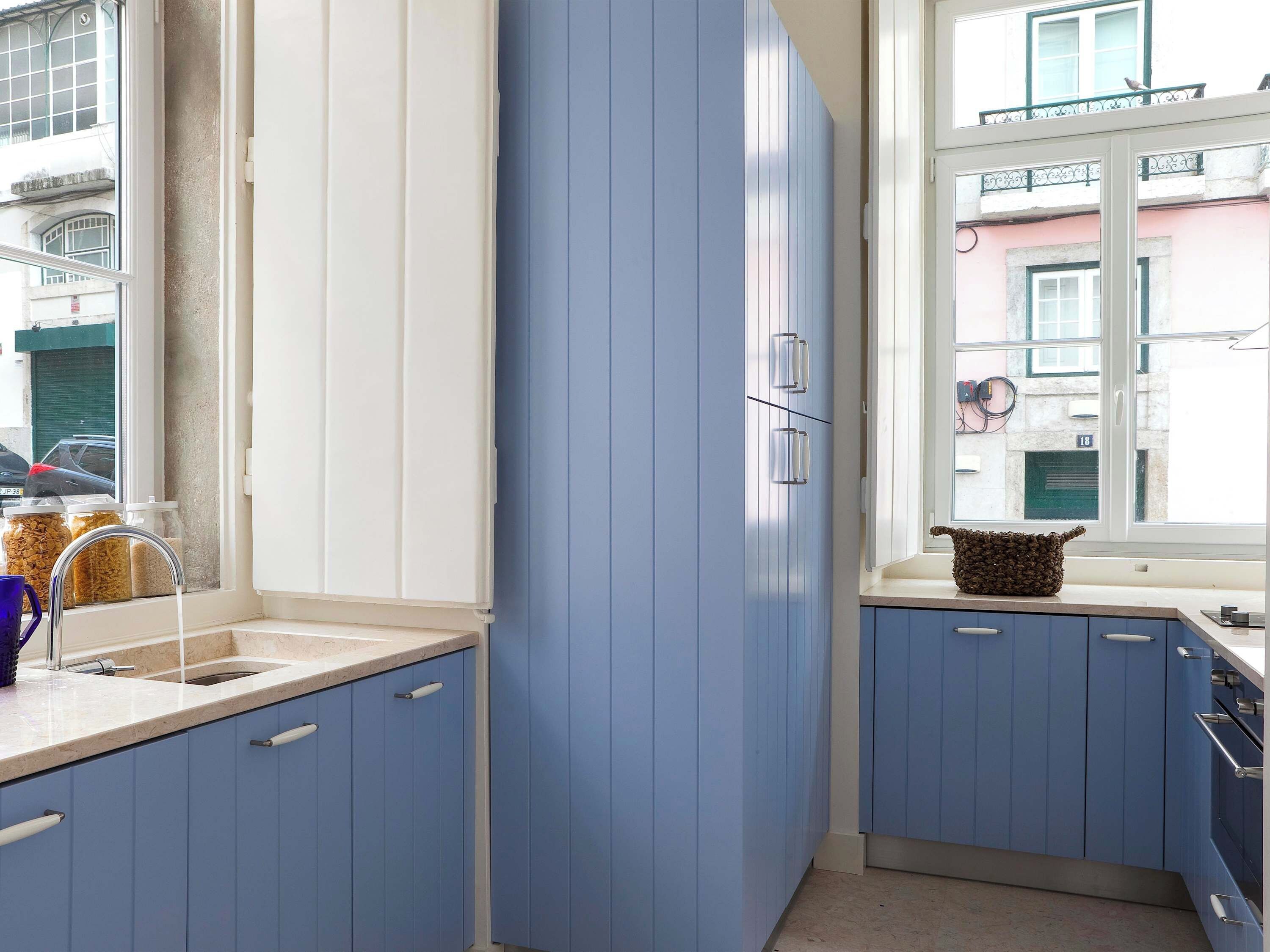 A kitchen with blue cabinets, a window with a view of the street, and a sink with a faucet.