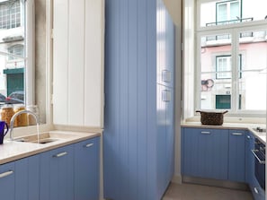 A kitchen with blue cabinets, a window with a view of the street, and a sink with a faucet. - Historic Lisbon Apartment Near Chiado (Lisbon)