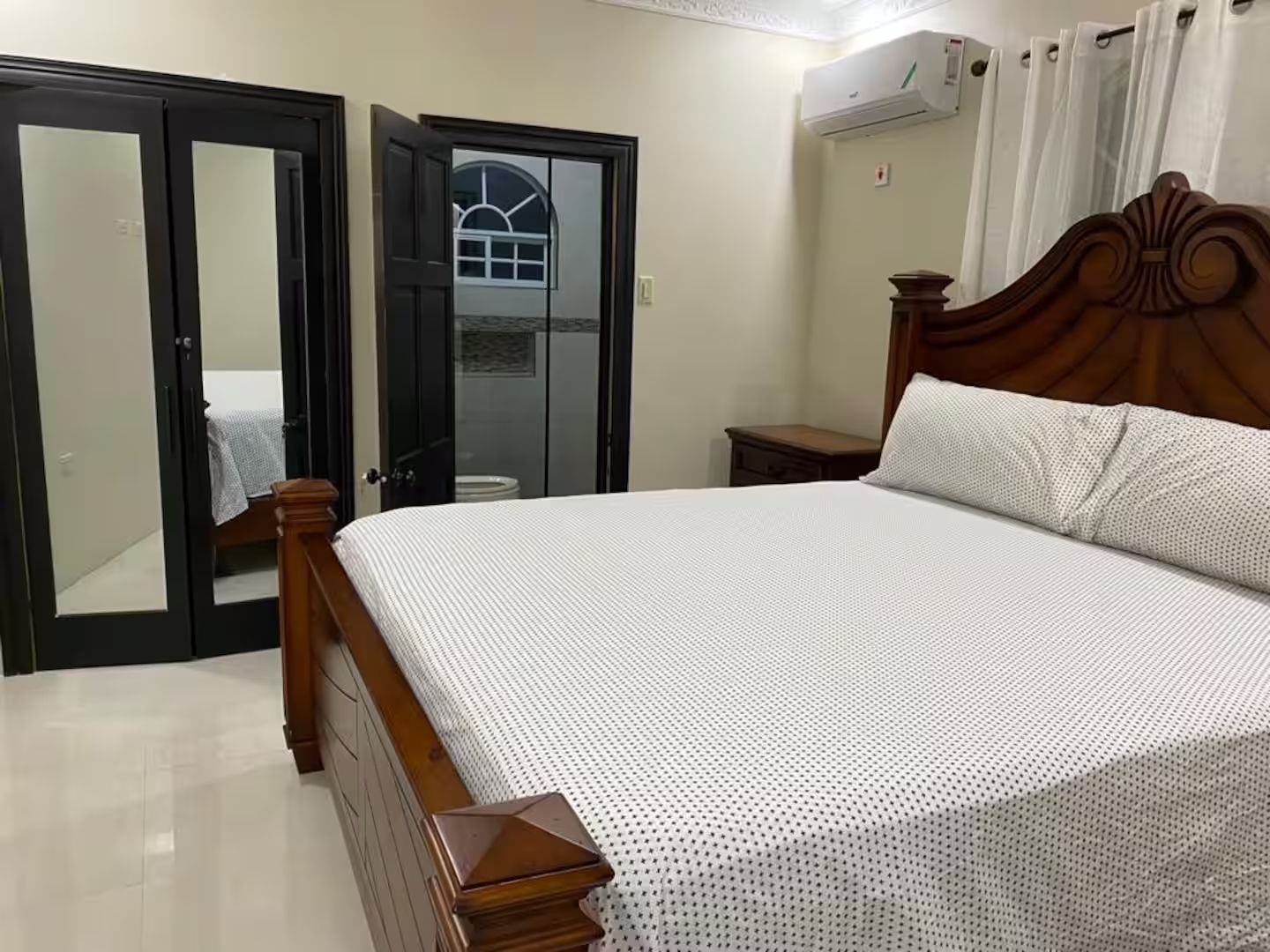 A bedroom with a wooden bed, a wardrobe, and a bathroom visible through an open door.