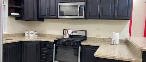 A kitchen with dark cabinets, a stainless steel microwave, a gas stove, and granite countertops.