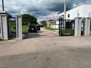 Un carrer d'accés tancat per una reixa que condueix a una propietat residencial amb un cotxe a l'interior.