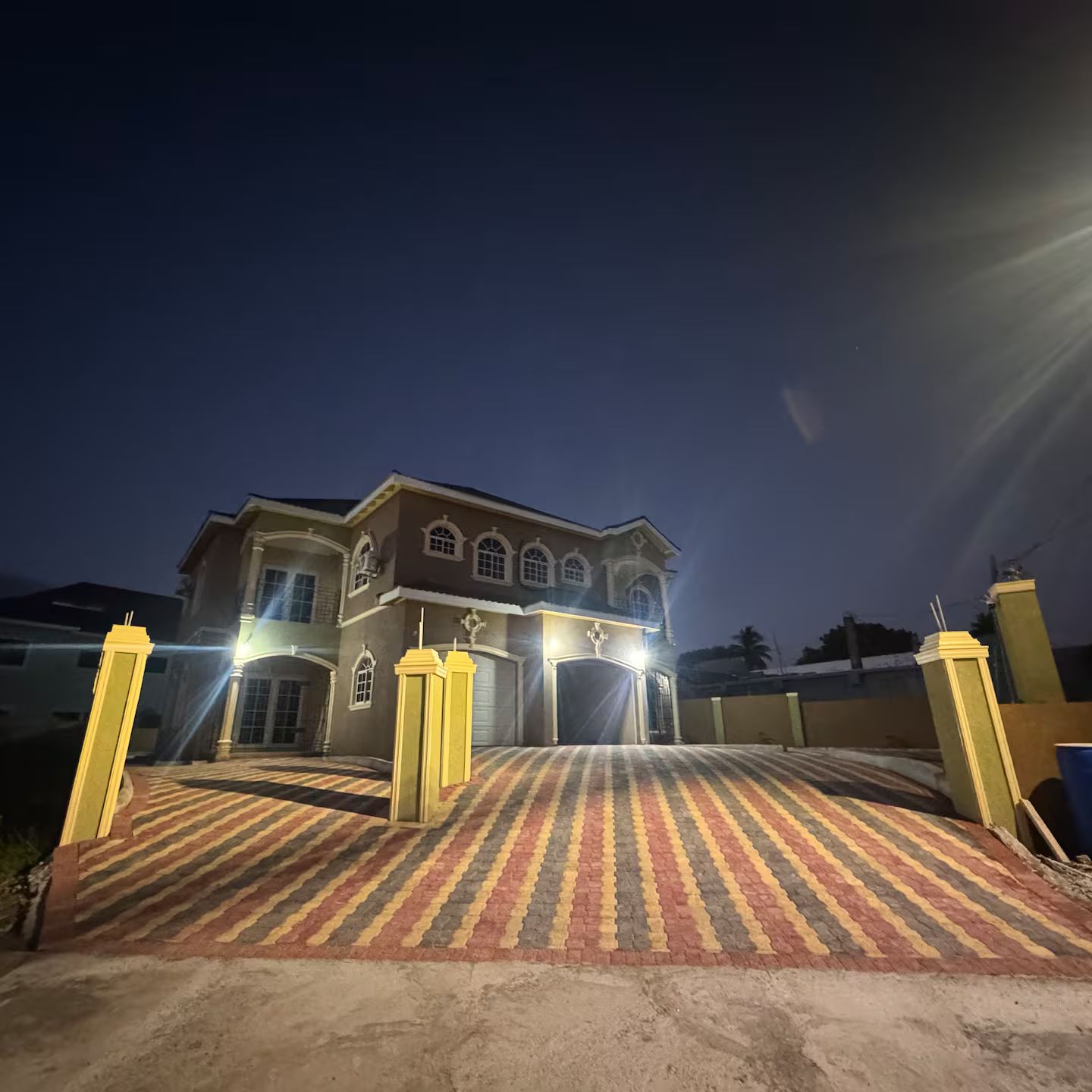 Una casa grande de dos pisos con un camino de entrada cerrado por una reja y un sendero con diseño.