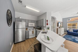 A modern kitchen with stainless steel appliances, a central island, and a dining area with a blue sofa. - Emerald Island Corner Townhome  2 King Suites (Kissimmee)