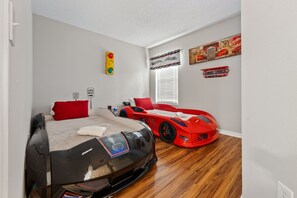 Um quarto com uma cama, um carro esportivo vermelho e uma parede com placa de limite de velocidade.