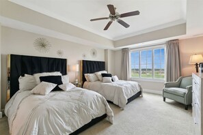 A bedroom with two beds, a ceiling fan, a window with a view, and a chair.