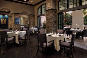 Ein Restaurant mit Steinsäulen, dunklem Holzboden und gedeckten Tischen.