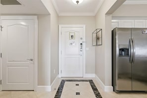 A hallway with a white door, a door with a photo and a lock, and a stainless steel refrigerator.