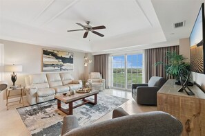 Una sala de estar amplia con ventilador de techo, un ventanal con vistas, un sofá, una mesa de centro y un televisor.