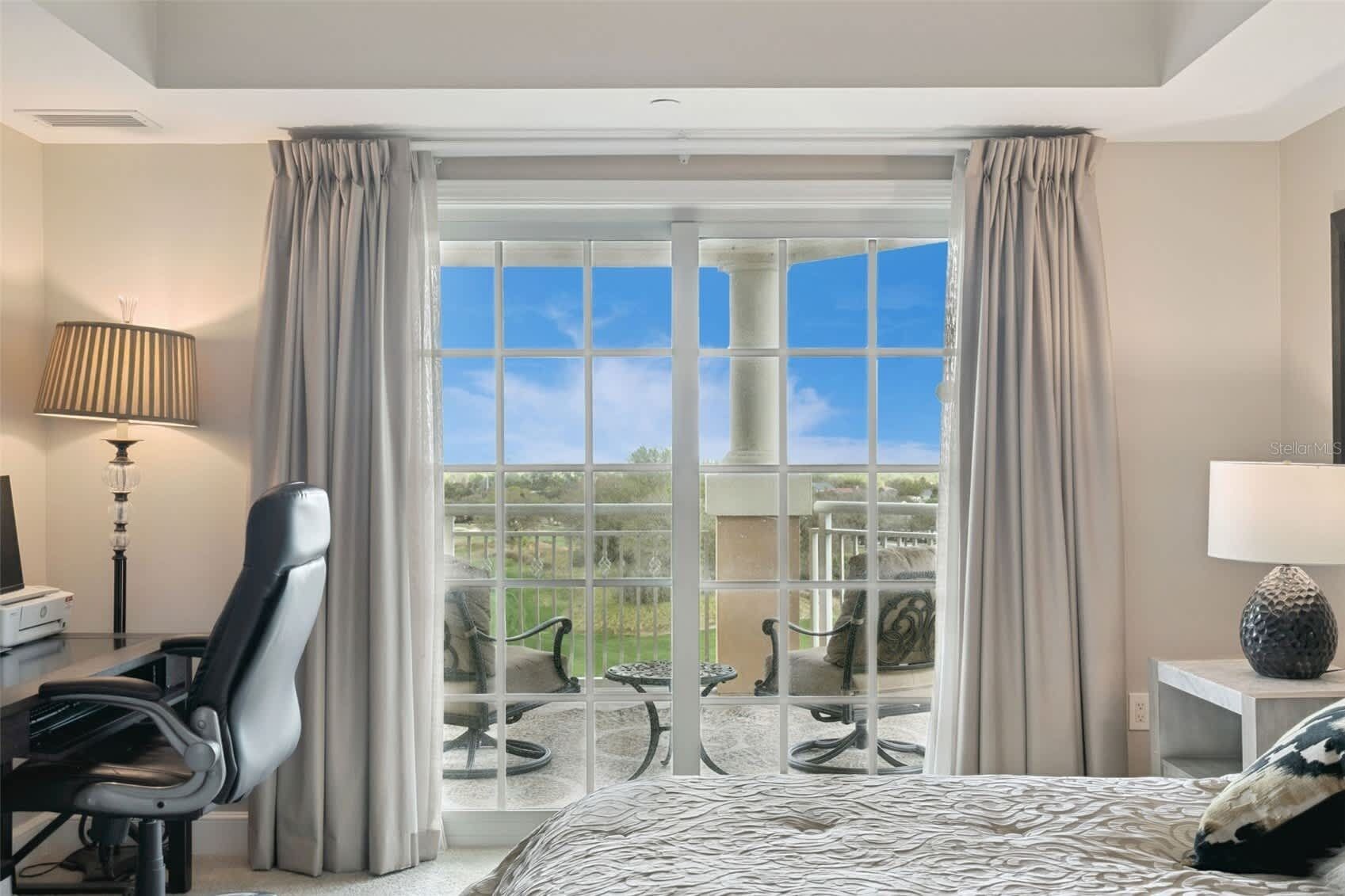 Une chambre d’hôtel équipée d’un lit, d’un bureau, d’une chaise, d’une lampe et offrant une vue sur l’extérieur grâce à une porte vitrée.