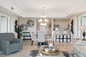 A modern living room with a grey sofa, a dining area with a chandelier, and a kitchen in the background.