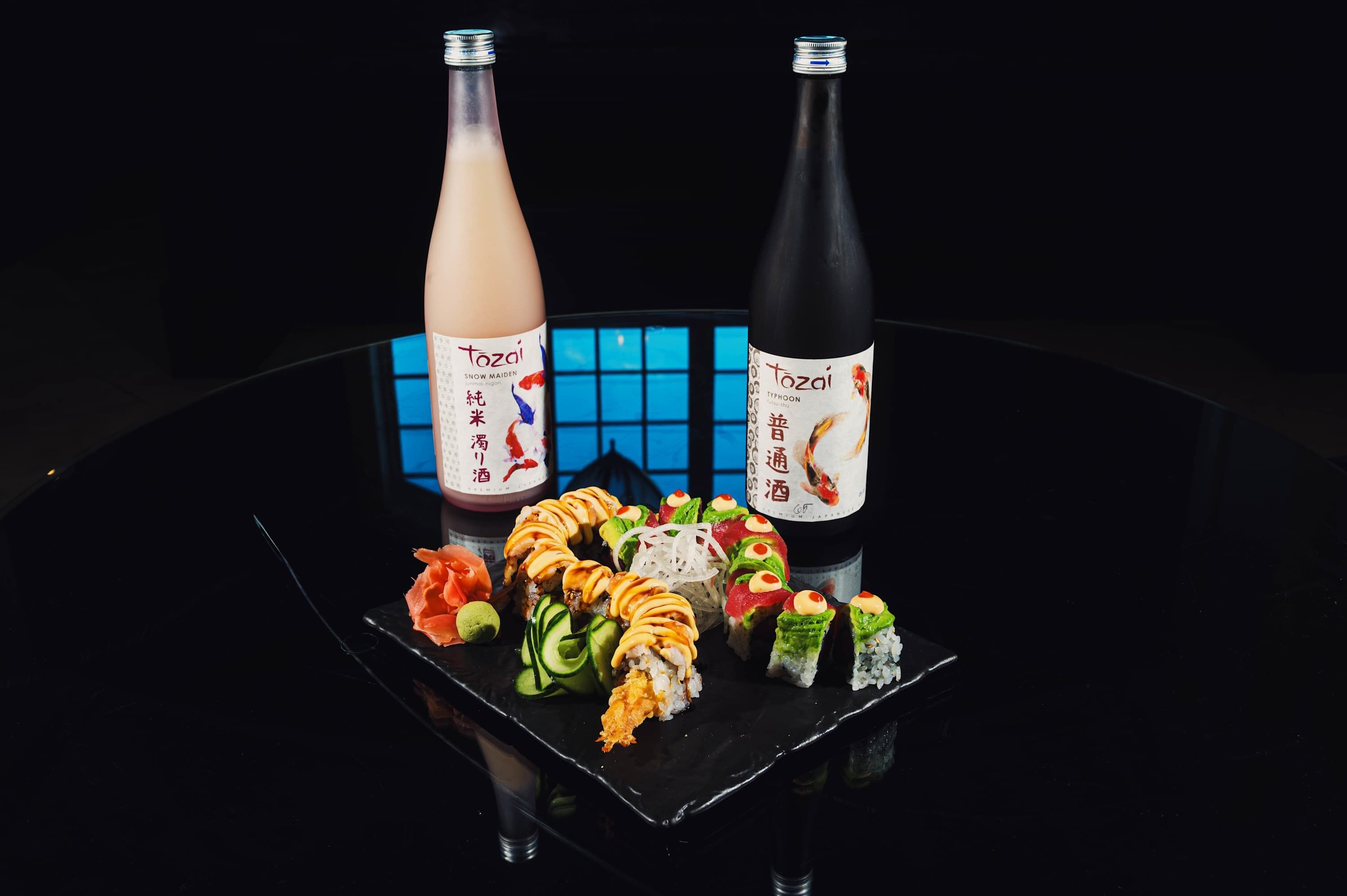 A table with various sushi dishes and two bottles of sake.