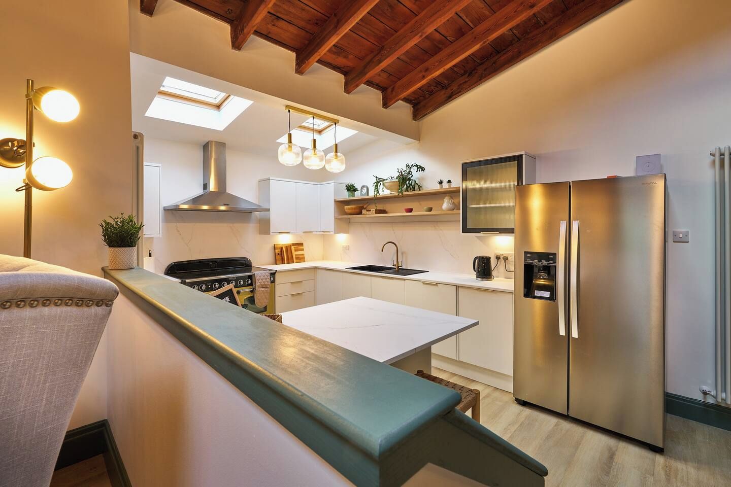 Una cocina moderna con una isla central, horno empotrado, electrodomésticos de acero inoxidable y techo de madera.